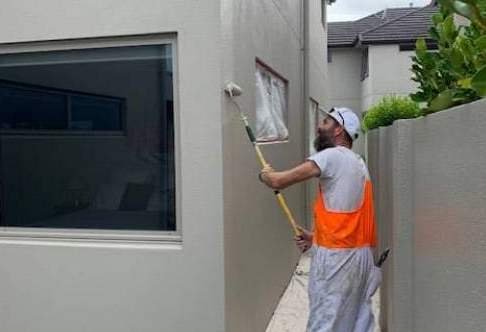Un imbianchino durante la tinteggiatura esterna di una casa. Gli interventi sugli esterni implicano un costo orario pi&ugrave; alto.